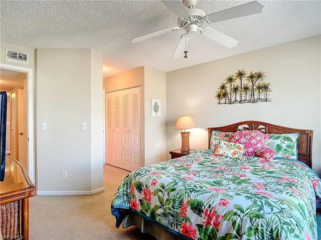 Bedroom featuring light carpet, ceiling fan, a closet, and a textured ceiling