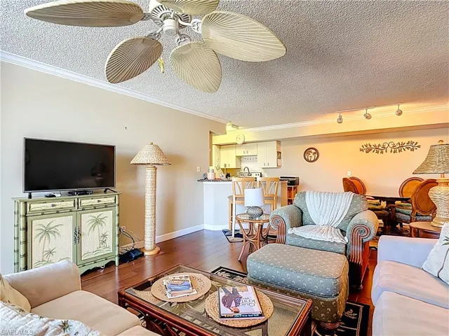 Living room featuring crown molding, dark wood finished floors, a textured ceiling, and ceiling fan