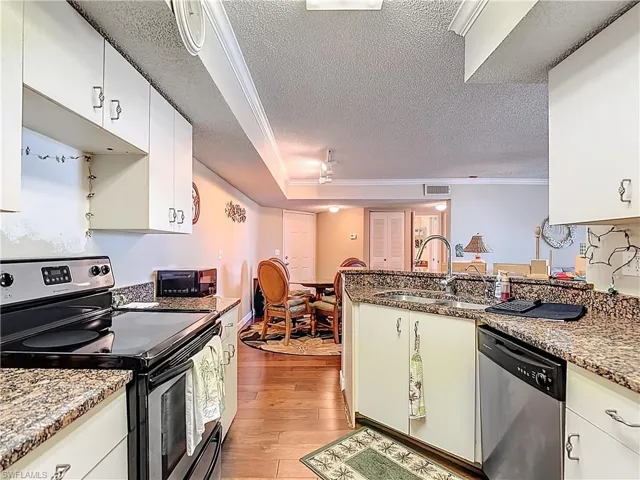 Kitchen featuring ornamental molding, stainless steel appliances, a textured ceiling, a peninsula, and light stone counters