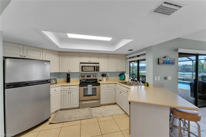 Kitchen featuring light tile patterned flooring, stainless steel appliances, a raised ceiling, and kitchen peninsula