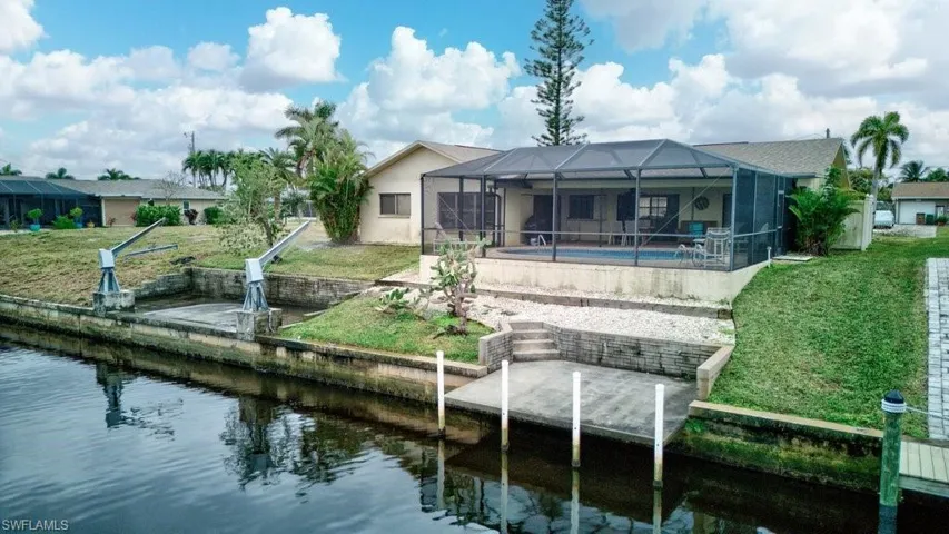Rear view of house featuring glass enclosure, a water view, a yard, and a patio
