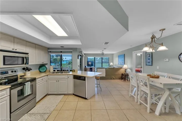 Kitchen with decorative light fixtures, a tray ceiling, stainless steel appliances, light tile patterned floors, and a breakfast bar area