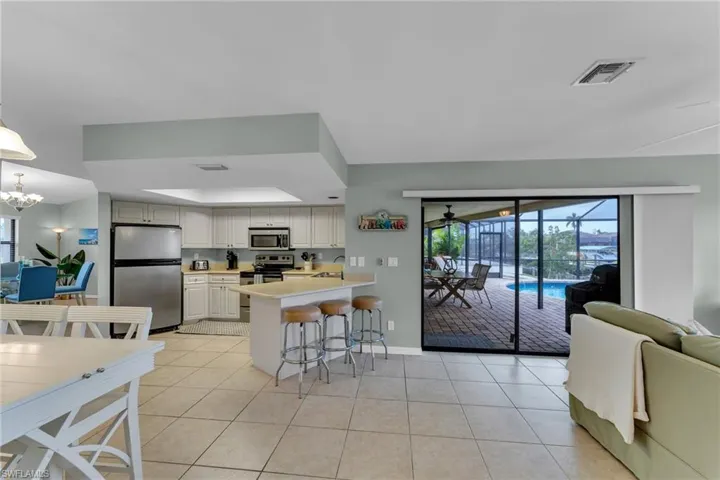 Kitchen featuring light tile patterned floors, a kitchen bar, appliances with stainless steel finishes, a raised ceiling, and hanging light fixtures