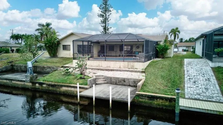 Back of house with a water view, a yard, a patio area, and glass enclosure