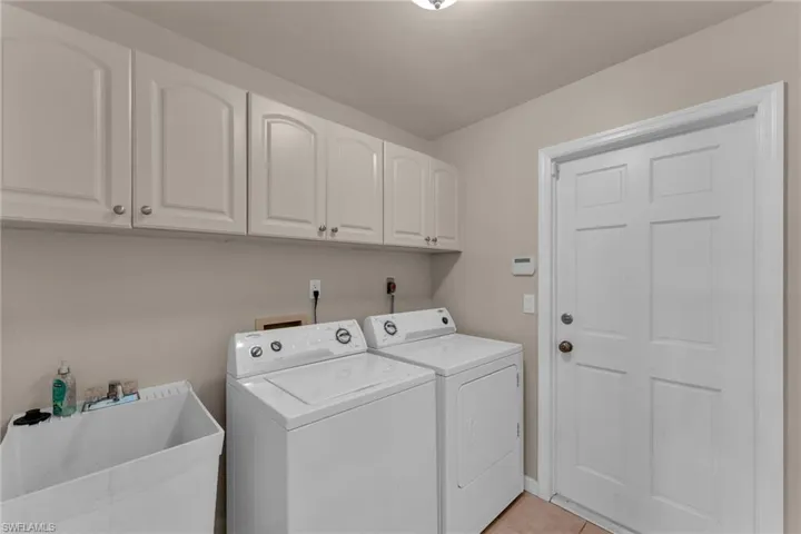 Laundry room with washer and dryer, light tile patterned flooring, sink, and cabinets