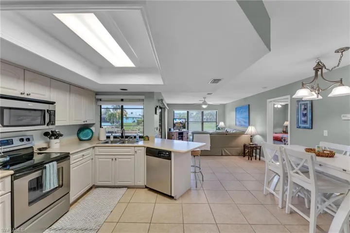 Kitchen featuring ceiling fan with notable chandelier, stainless steel appliances, sink, kitchen peninsula, and a raised ceiling
