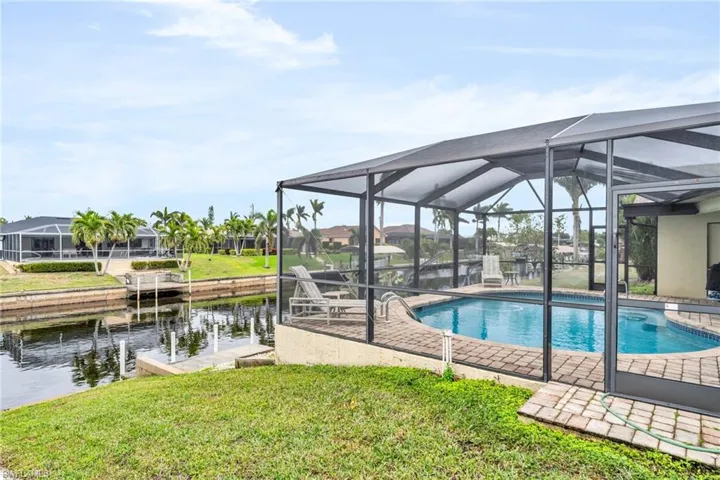 View of swimming pool with glass enclosure, a water view, and a yard