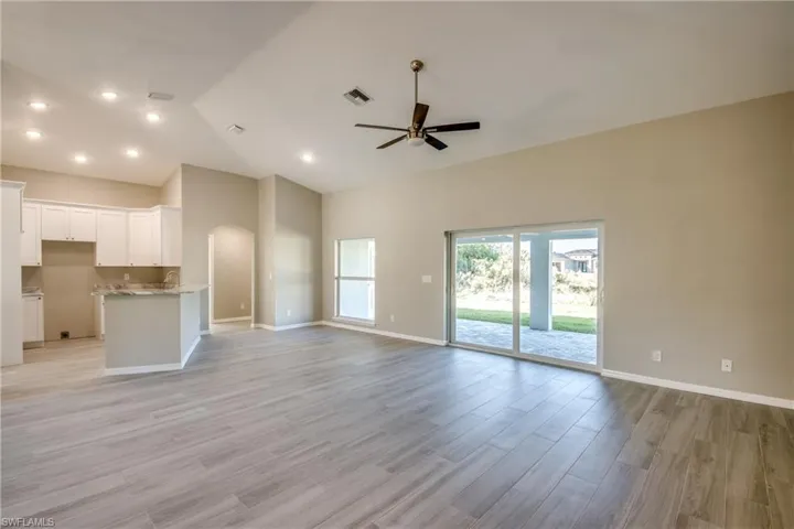 Unfurnished living room featuring arched walkways, light wood finished floors, ceiling fan, and high vaulted ceiling
