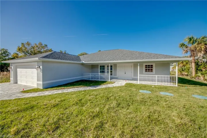 Ranch-style home featuring stucco siding, a garage, a front yard, covered porch, and roof with shingles