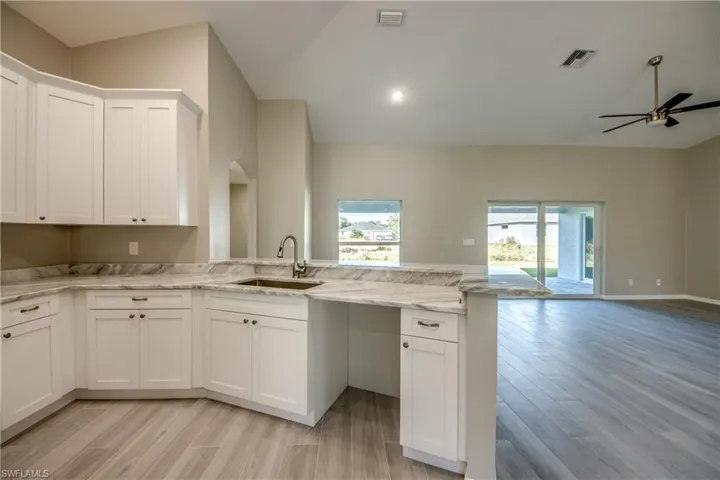 Kitchen featuring a peninsula, white cabinets, open floor plan, light stone counters, and light wood finished floors