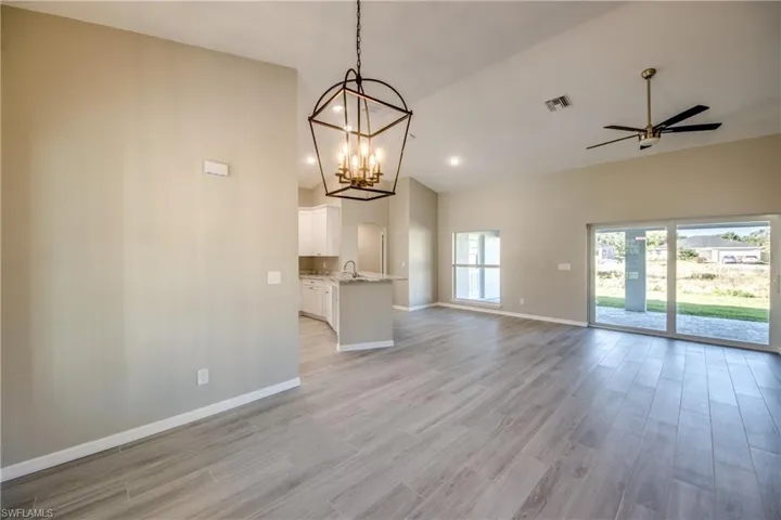 Unfurnished living room with ceiling fan, light wood finished floors, a chandelier, recessed lighting, and high vaulted ceiling