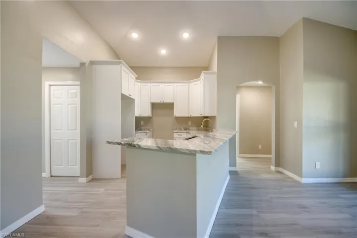 Kitchen with arched walkways, white cabinetry, light stone countertops, light wood-style floors, and recessed lighting