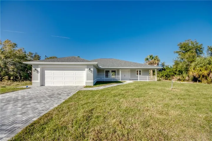 Ranch-style house featuring covered porch, a front lawn, stucco siding, decorative driveway, and a garage