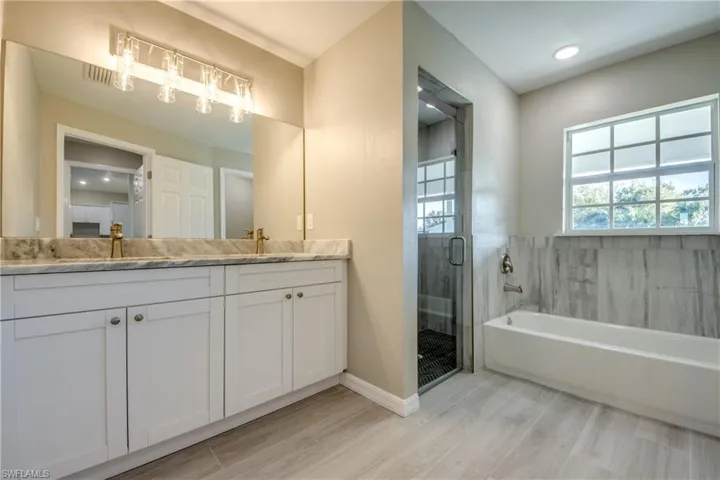 Bathroom with double vanity, a shower stall, a bath, light wood-style floors, and recessed lighting