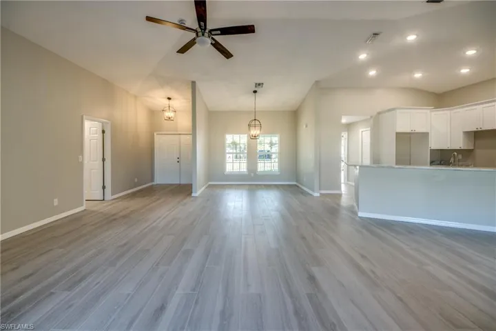 Unfurnished living room featuring light wood-style floors, lofted ceiling, ceiling fan, a chandelier, and recessed lighting