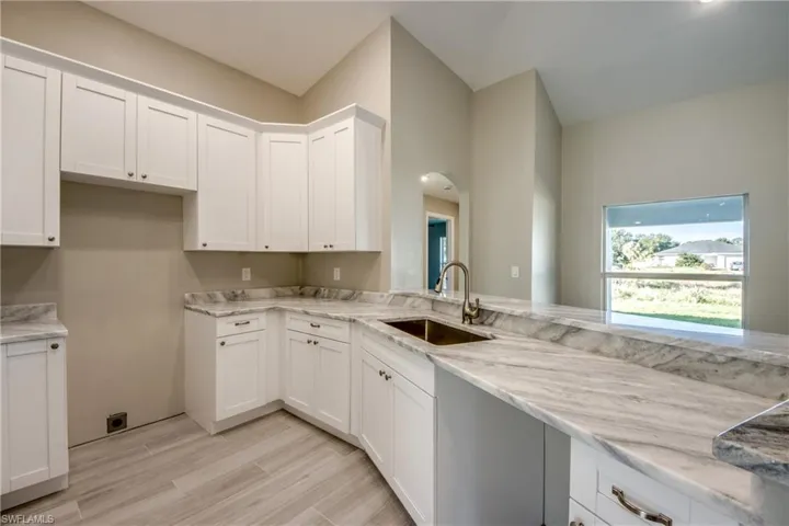 Kitchen featuring white cabinets, wood finish floors, and light stone counters