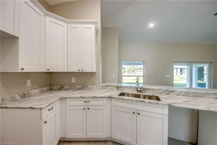 Kitchen with white cabinets, light stone countertops, and recessed lighting