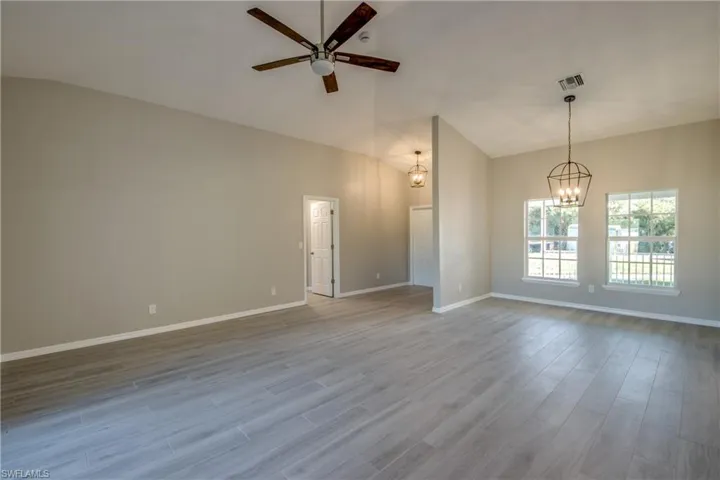 Empty room with lofted ceiling, wood finished floors, a chandelier, and a ceiling fan