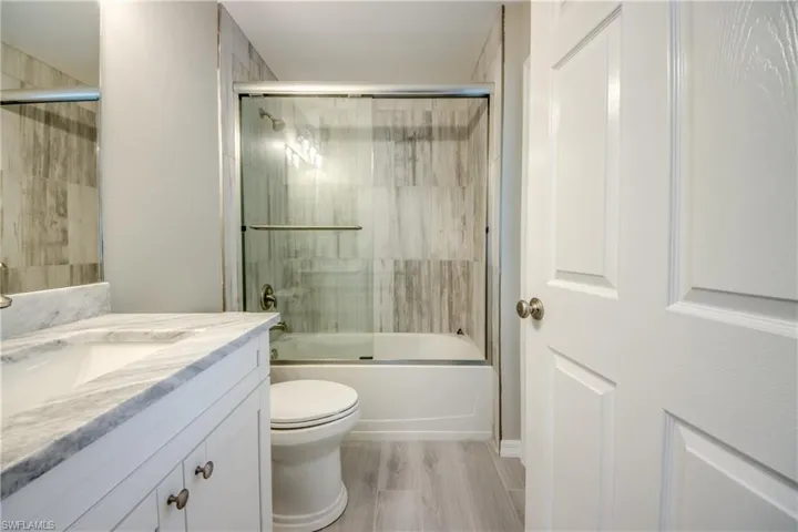Full bathroom featuring enclosed tub / shower combo, vanity, and light wood-style flooring