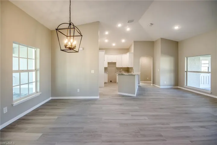 Kitchen with white cabinets, open floor plan, pendant lighting, arched walkways, and light wood finished floors