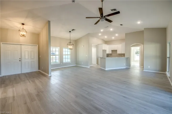 Unfurnished living room with plenty of natural light, a chandelier, a ceiling fan, light wood-type flooring, and lofted ceiling
