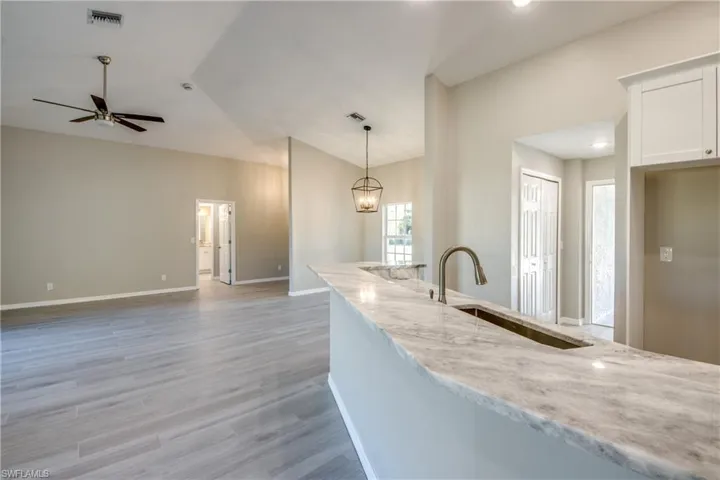 Kitchen with light stone counters, decorative light fixtures, light wood-type flooring, white cabinetry, and a ceiling fan