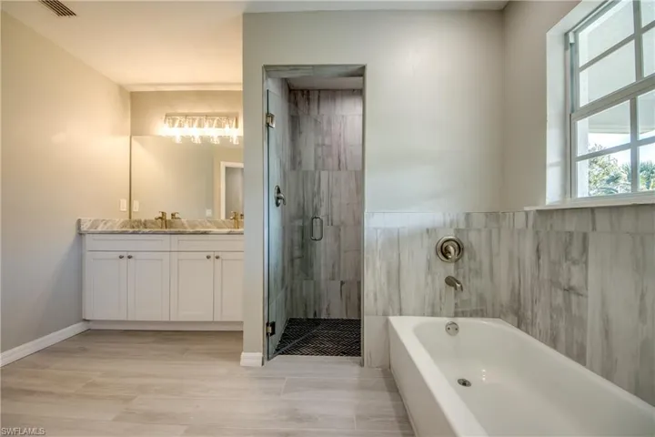 Bathroom featuring a bath, double vanity, a shower stall, and light wood finished floors