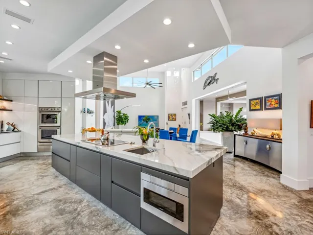 Kitchen featuring stainless steel microwave, sink, island exhaust hood, black electric cooktop, and a spacious island