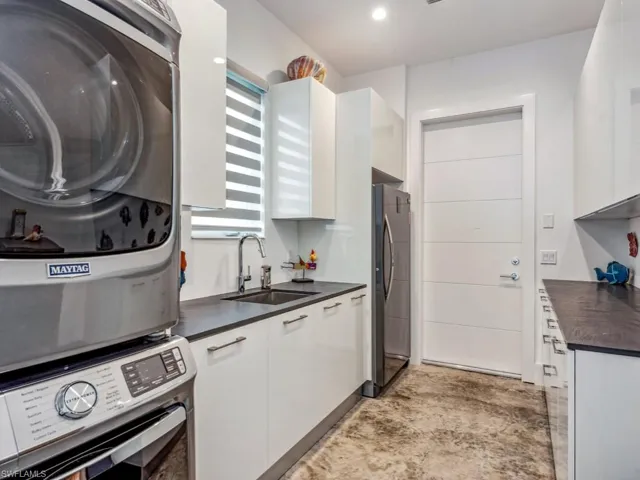 Kitchen with stacked washer / dryer, white cabinetry, sink, and stainless steel refrigerator