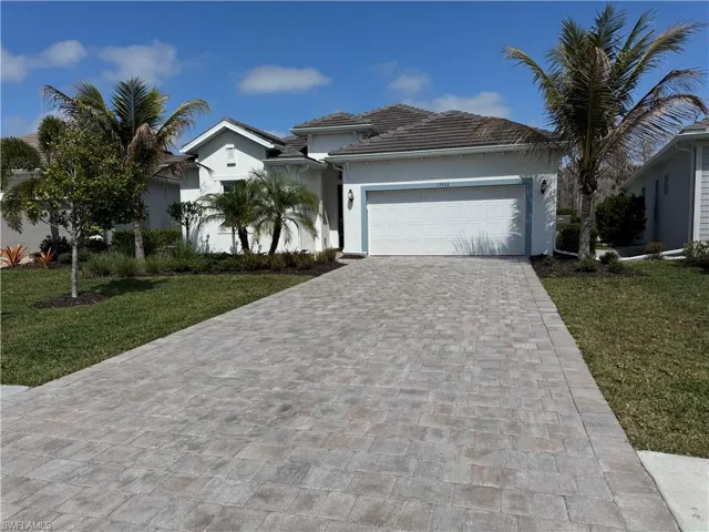 View of front of property with a front yard, a garage, decorative driveway, and stucco siding