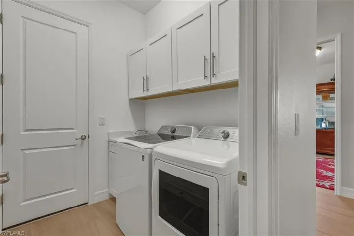 Laundry area featuring cabinet space, light plank tile floors, tub and washer and clothes dryer, Door leads to garage.