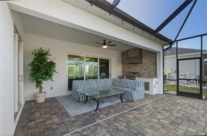 Outdoor resort-style living area with outdoor kitchen, panoramic-screened lanai featuring pavers, sliding doors, 2 side screen doors and a ceiling fan.