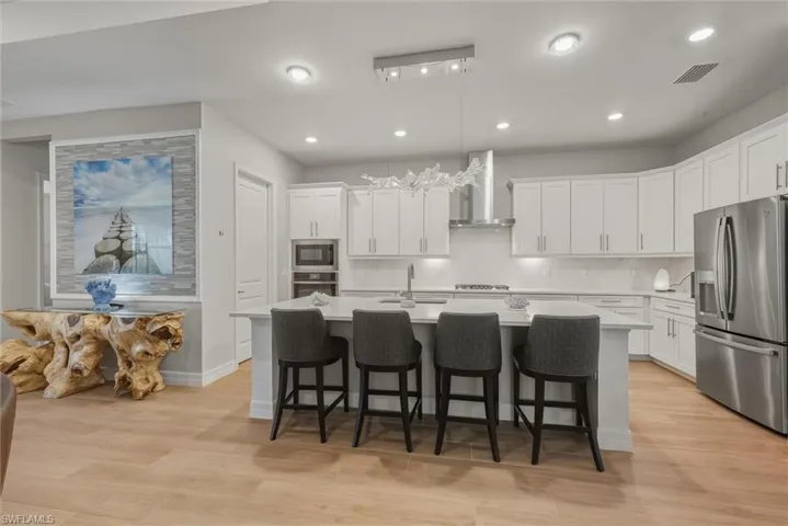 Kitchen featuring GE stainless steel appliances, a breakfast bar area, walk-in pantry, tasteful bright backsplash, under cabinet luighting, white cabinetry, and ultra-modern hanging light fixture. Decorative wall with modern lighted artwork and table.