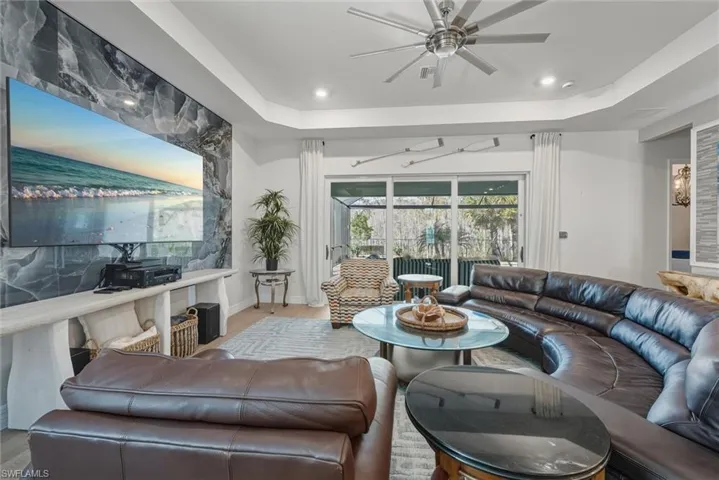 Living room featuring a decorative wall, ceiling fan, a tray ceiling, sliding doors with modern side drapes and tile plank floors