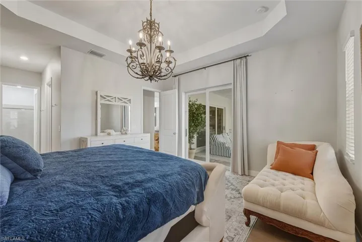 Primary Bedroom Suite with sliding door access to lanai, a modern chandelier, and a tray ceiling