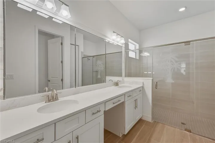 Primary bathroom featuring double sink quartz vanity, plank tile flooring, bright modern lighting and a glass enclosed shower stall