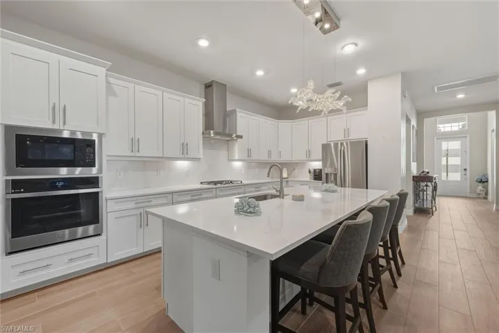 Kitchen with GE appliances with stainless steel finishes, a kitchen breakfast bar, white cabinetry, ultra-modern hanging light fixture, recessed lighting and tile plank flooring