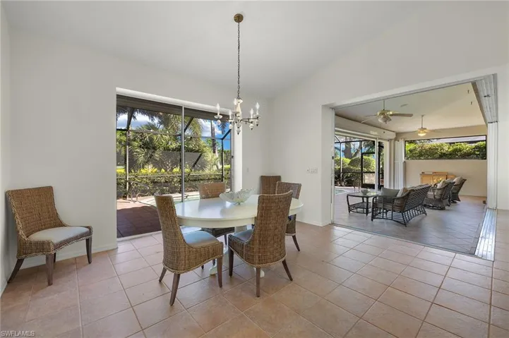Dining area with ceiling fan with notable chandelier, a healthy amount of sunlight, light tile patterned floors, and vaulted ceiling