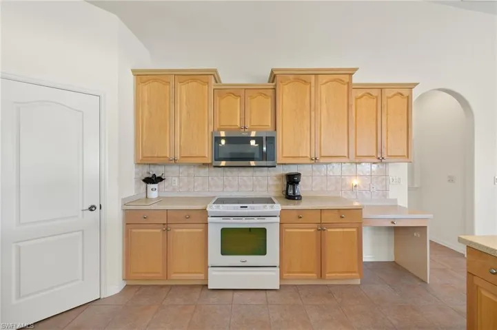 Kitchen featuring white electric range, backsplash, vaulted ceiling, and light tile patterned floors