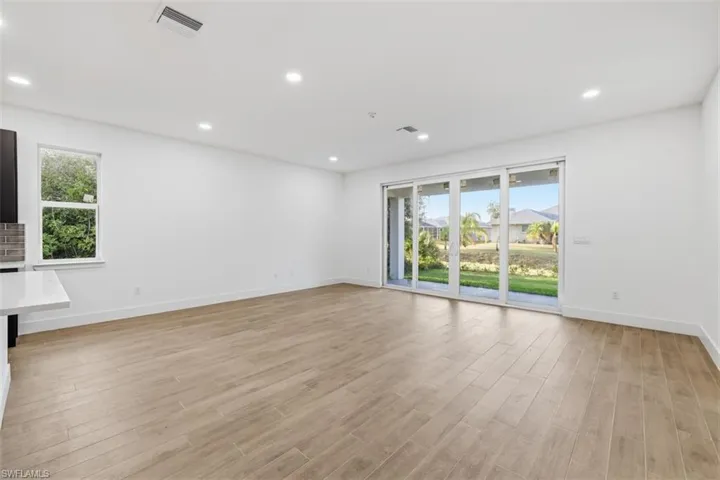 Expansive interior space featuring wood-finish flooring, recessed lighting, and a window with verdant landscaping