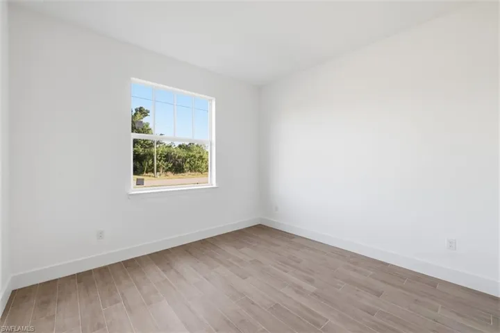 Bright room featuring a large window, wood-finish flooring, white walls, and white baseboards