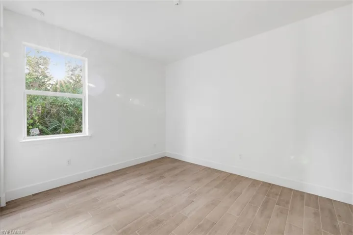 Room featuring a bright window with exterior landscaping, wood-finish flooring, white baseboards, and neutral wall finishes