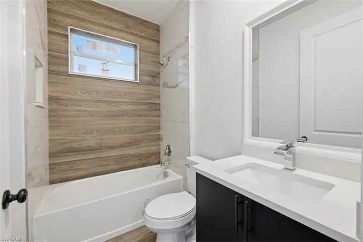 Bathroom featuring a bathtub with a wood-look tiled surround, a built-in shower niche, and a window