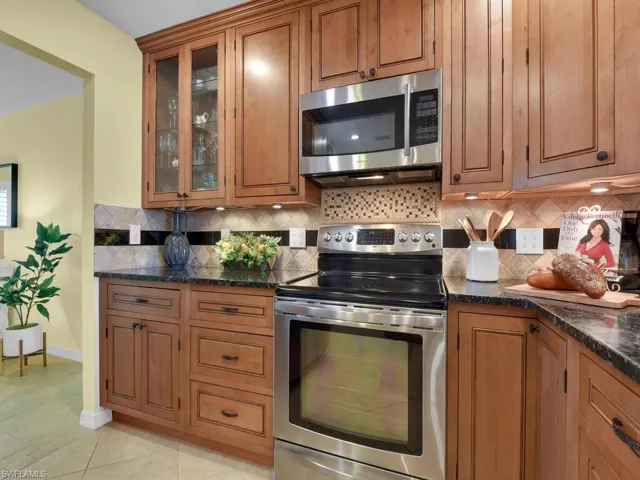 Kitchen with light tile patterned floors, stainless steel appliances, tasteful backsplash, and dark stone counters
