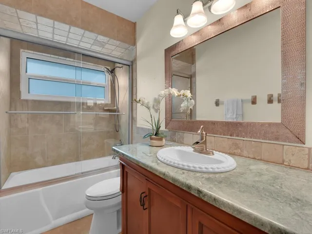 Full bathroom with toilet, bath / shower combo with glass door, and vanity