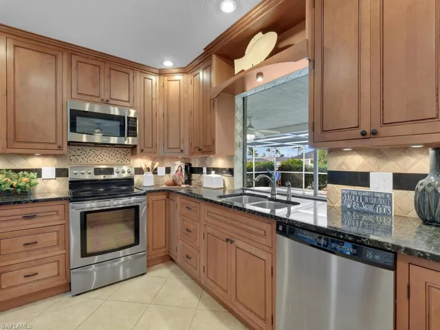 Kitchen featuring light tile patterned flooring, stainless steel appliances, dark stone countertops, and sink
