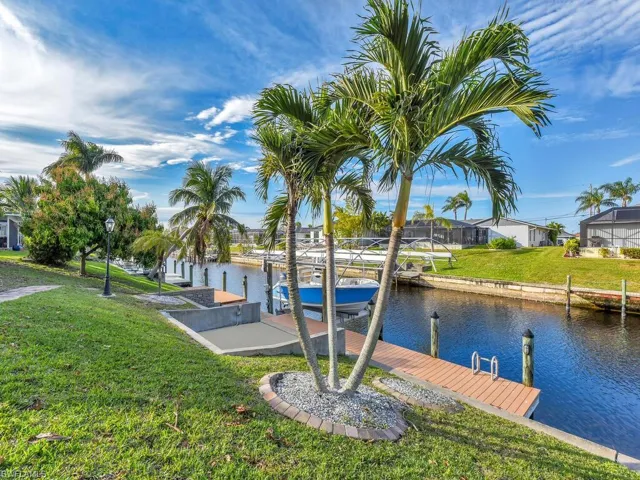 View of dock with a water view, a lawn, and glass enclosure