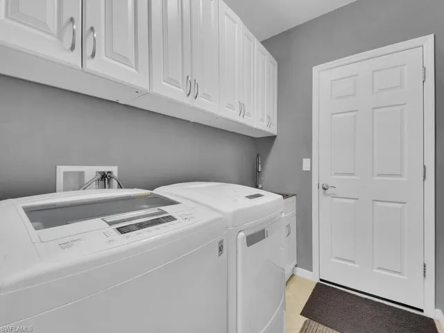 Clothes washing area with light tile patterned floors, sink, cabinets, and washing machine and dryer