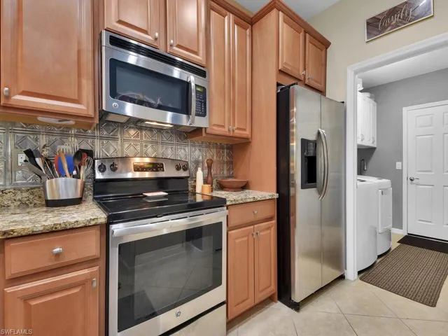 Kitchen with backsplash, light tile patterned floors, appliances with stainless steel finishes, and light stone countertops