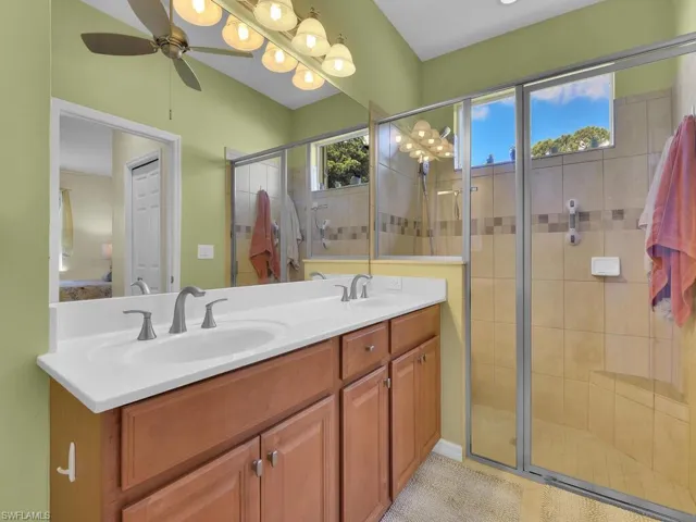 Bathroom featuring vanity, a shower with shower door, ceiling fan, and tile patterned floors